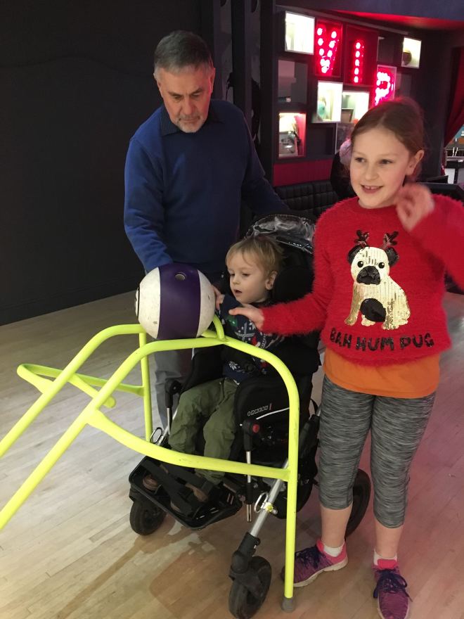 Quinns pushing a bowling ball down the ramp with his Big Sister and Opa