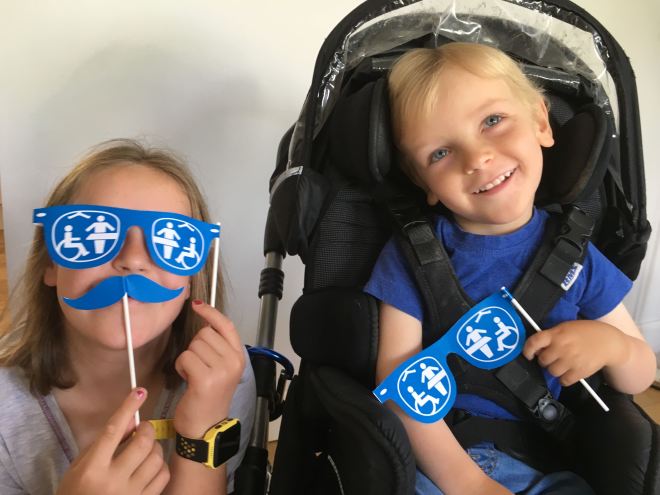 Photo of Quinns holding Changing Places paper glasses in his hand beside his Big Sister who is holding glasses and moustache up to her face.