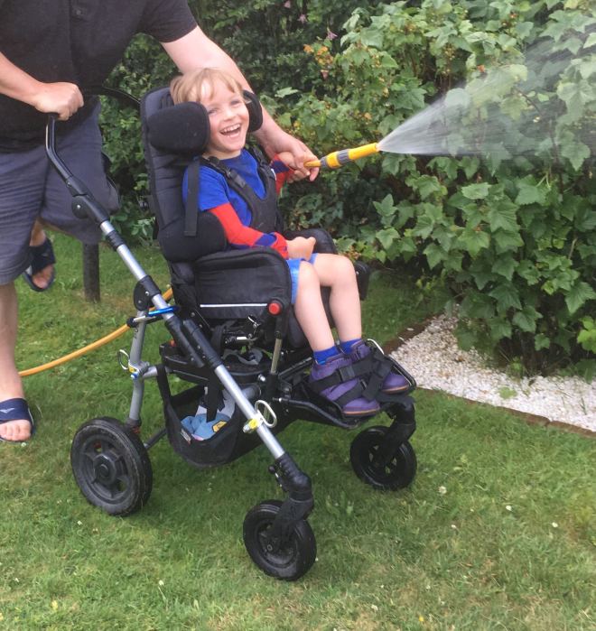 Photo of Quinns holding the hose to water fruit bushes supported from behind by Dad