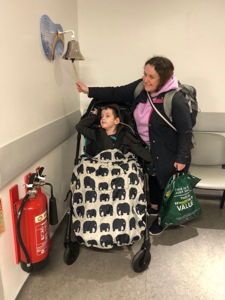 Quinns in his wheelchair reaches up to help pull the cord his mum is holding to ring the bell to signal the end of his long stay in hospital.