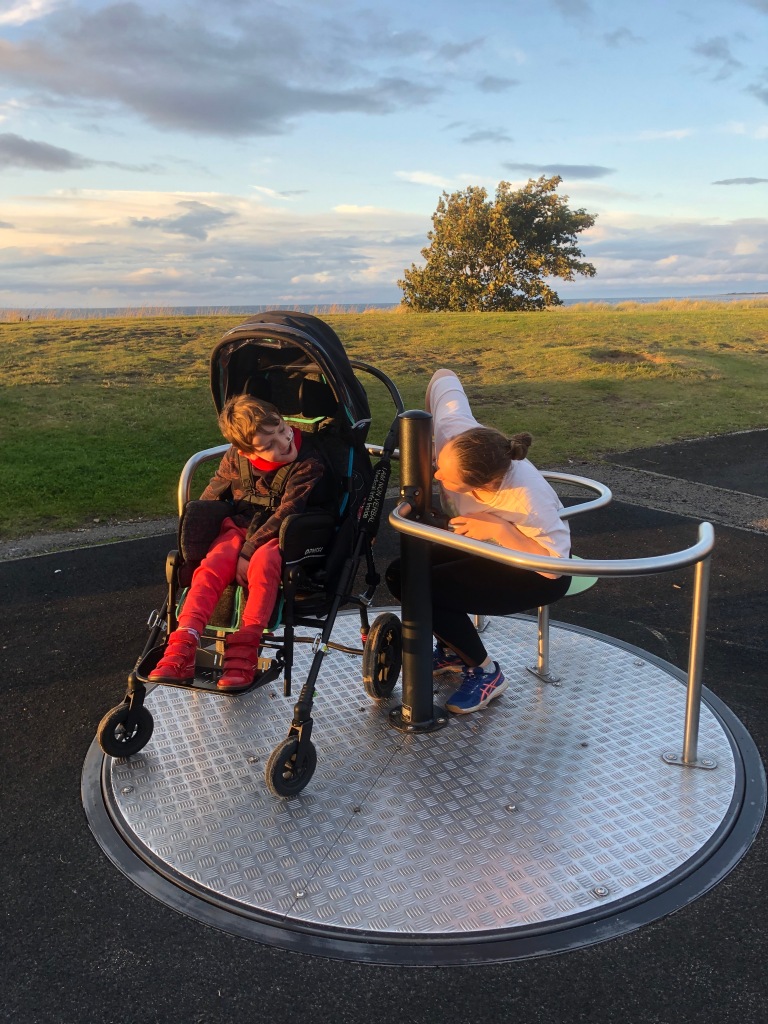 Quinns looks at his Big Sister as they spin on the accessible roundabout next to Nairn beach.