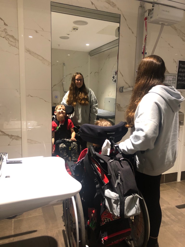 Quinns and his Big Sister posing in front of a mirror in the Changing Place toilet in Glasgow's Silverburn Shopping Centre.