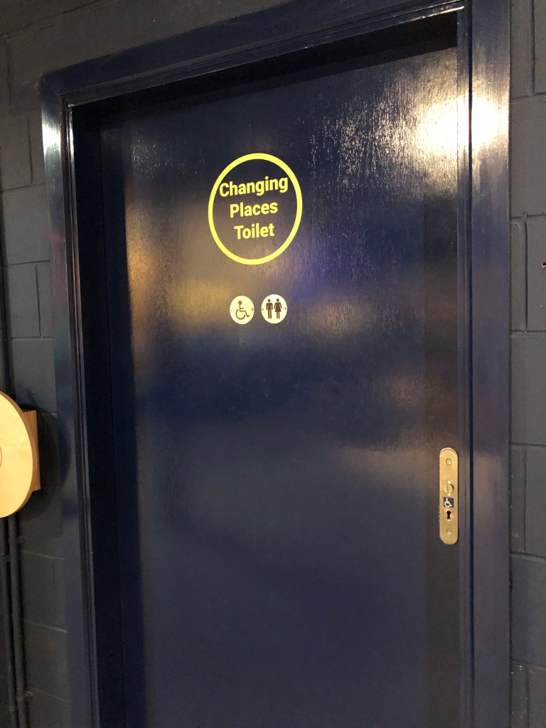 Dark blue toilet door with the words Changing Places toilet in bold yellow writing in the centre.