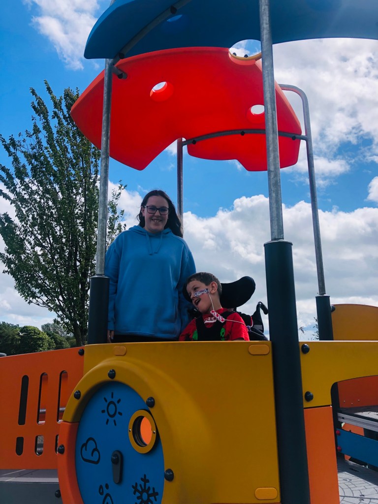 Anita and Quinns smile from on top of a piece of play equipment with sunshade above them.