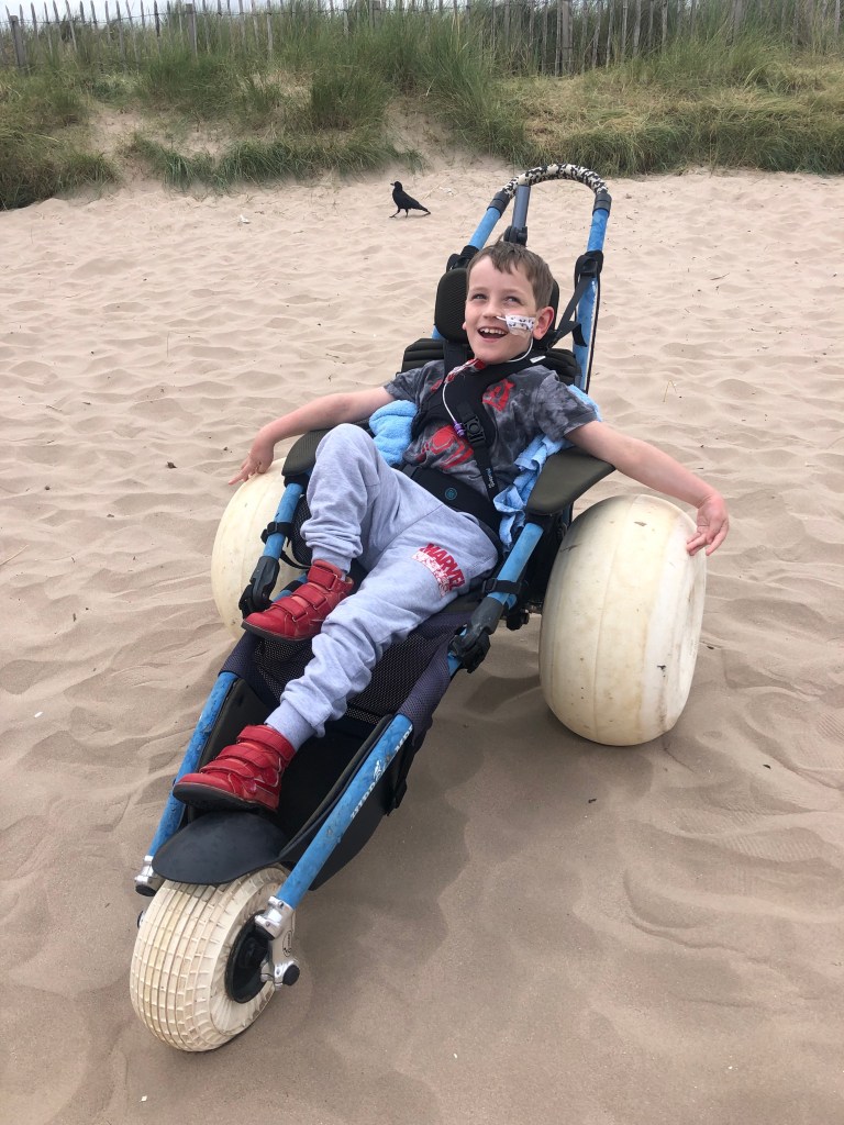 Quinns trying to smile but looking quite uncomfortable in a hippocampe beach wheelchair.