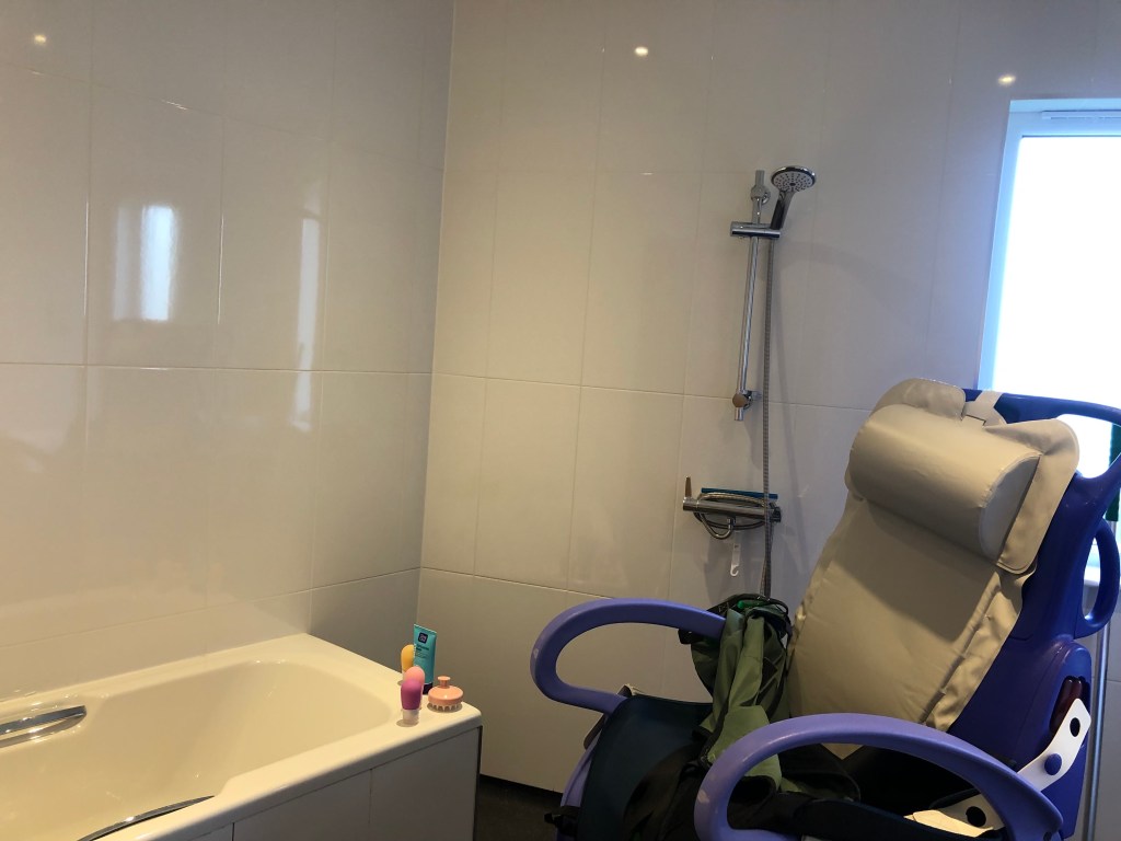 Wet room with separate bath and shower with a shower chair just in view.