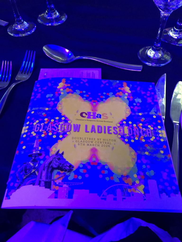 CHAS Glasgow Ladies Lunch booklet on the table at the event using Quinns art as the background