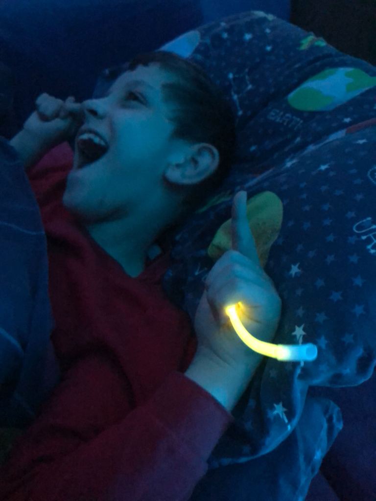 Quinns in his bed smiling holding a yellow glow stick.