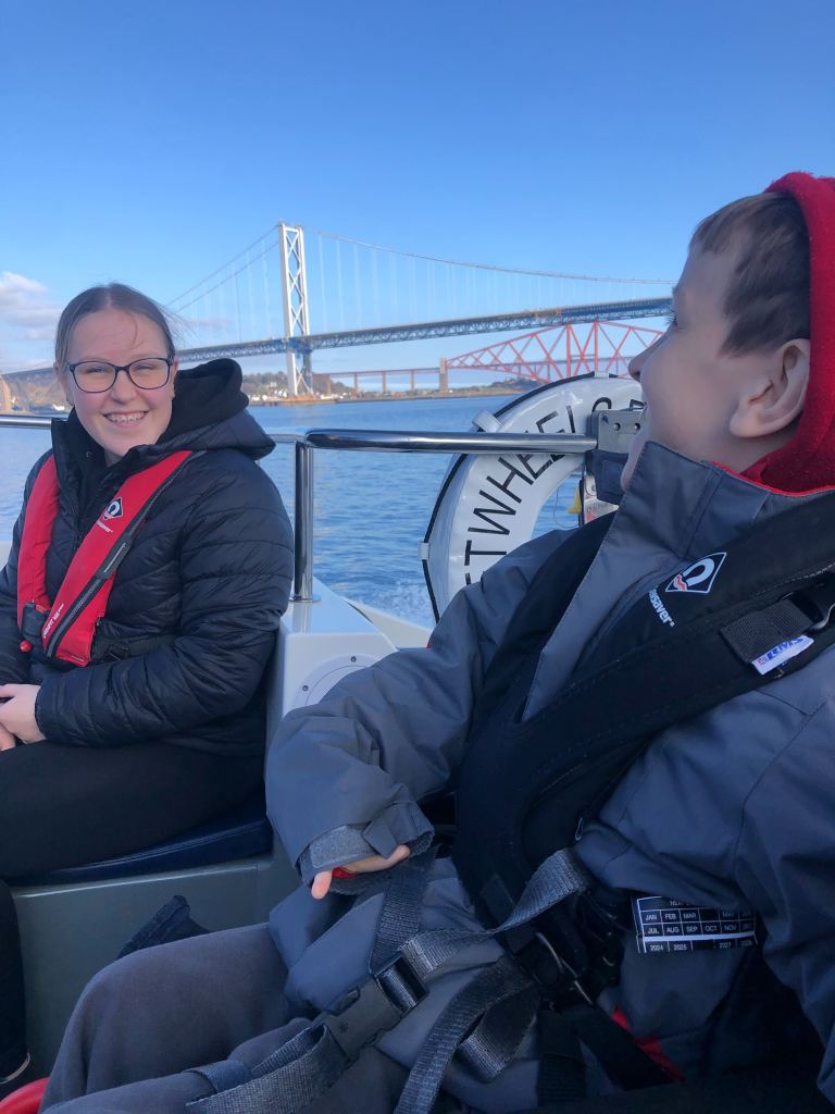 Quinns and his big sister look at each other as the Wet Wheels boat goes fast. The Forth Road and Rail Bridges can be seen in the background.