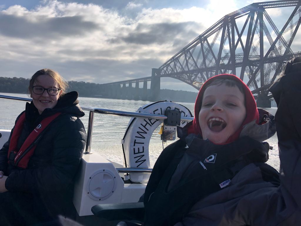 Quinns and his big sister smile on the Wet Wheels boat with the Forth Rail Bridge in the background.
