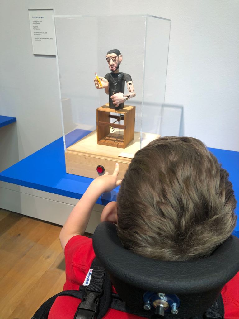 Quinns is reaching out to push a red button to make an automata work.