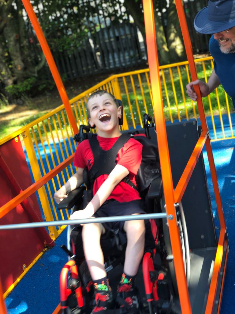 Quinns is smiling as he being pushed in a colourful wheelchair swing.