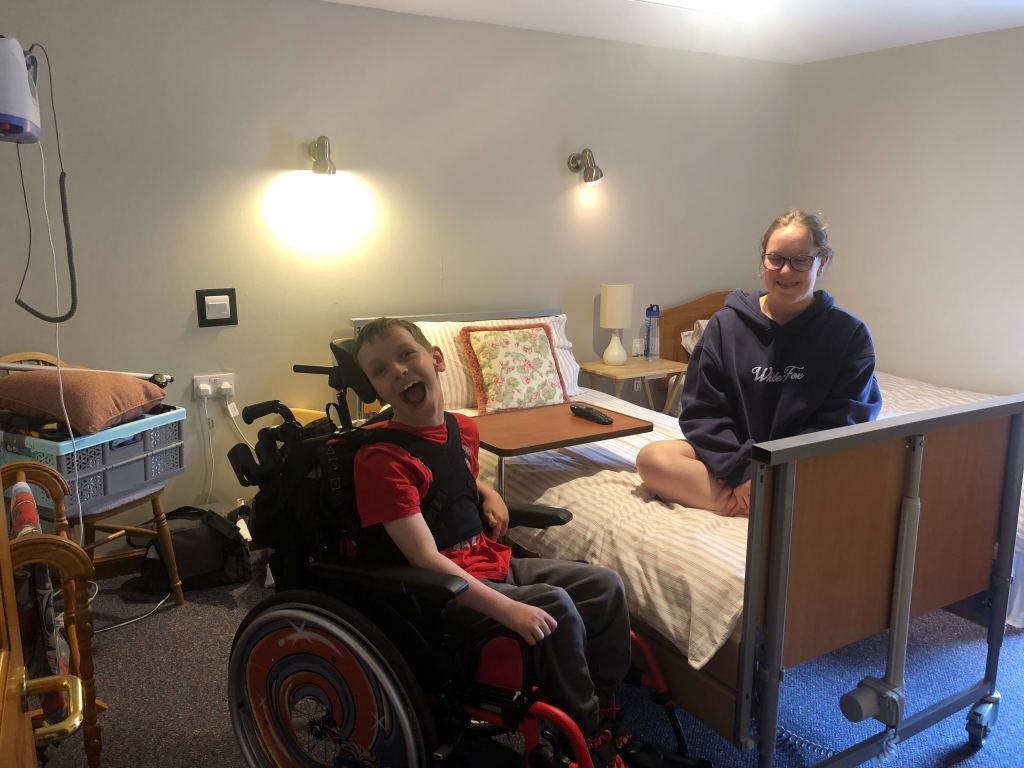 Quinns smiling beside his profiling bed in Gairn Cottage. Anita is sitting smiling on the bed.