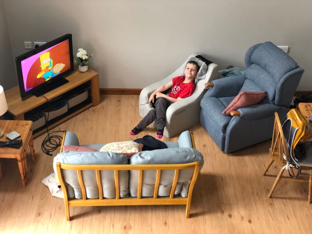 Camera looking down on Quinns sitting in his gravity chair in the living room of Gairn Cottage.