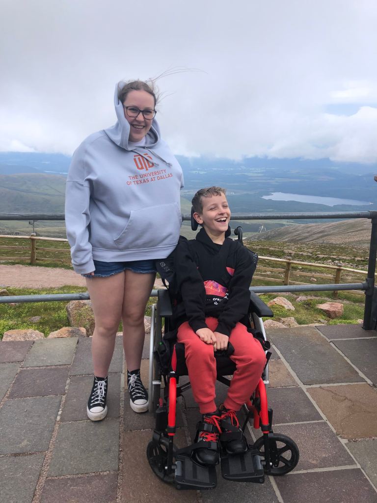 Quinns and Anita smiling but looking very windswept at the top of Cairngorm mountain.
