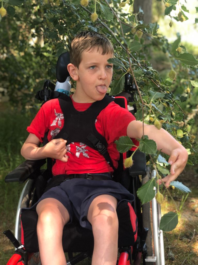 Quinns ticking his tongue out in concentration trying to grab the branch of tree he's sitting underneath.